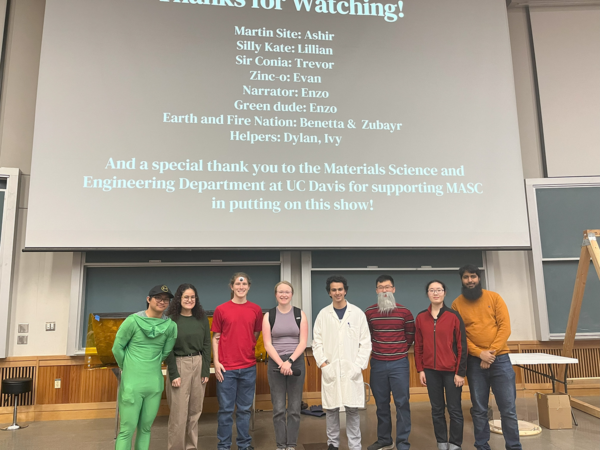 Group of eight students stand in a lecture hall in front of a screen with text that is thanking the audience for watching the materials magic show