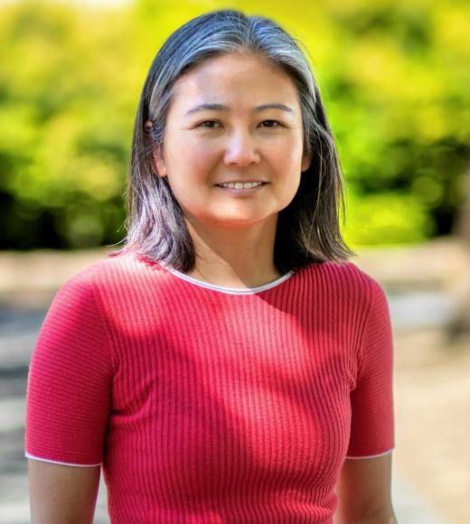 As Asian woman wearing a red shirt stands in front of a natural green background