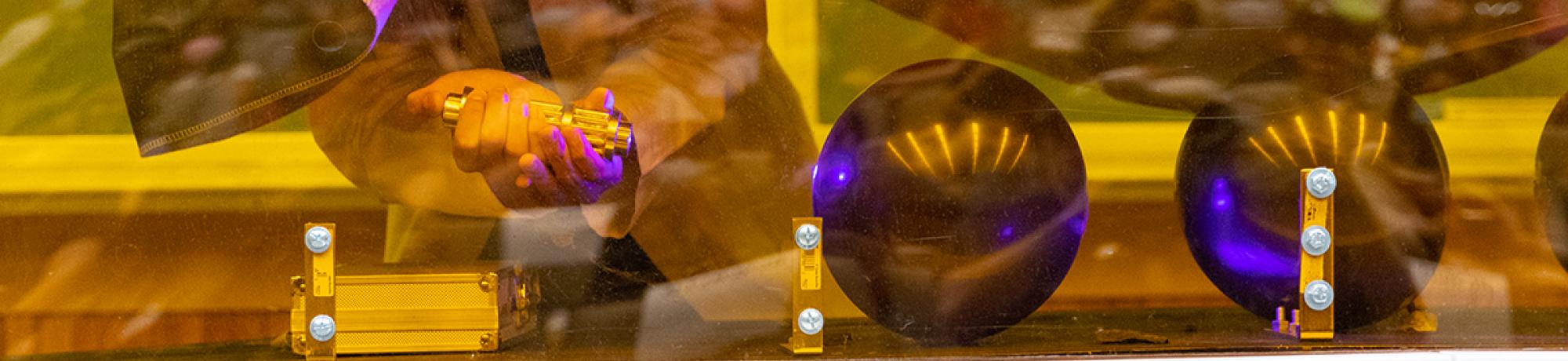 Someone underneath a black sheet or tarp points a light at black balls sitting on a folding table